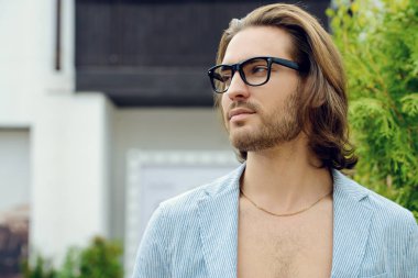 Mutlu genç adam modern giysiler içinde bir şehir sokak üzerinde duruyor ve kahve içiyor. Açık moda. 