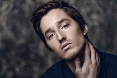 Yakın çekim mavi gömlekli koyu arka plan üzerinde koyu renk saçlı genç bir adam portresi. Erkek güzellik ve sağlık.