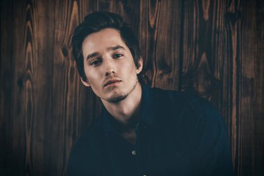 Vogue bir ahşap duvar bir kot gömlek bekliyor yakışıklı bir erkek modelinde bir kadeh. Erkek güzelliği, moda. 