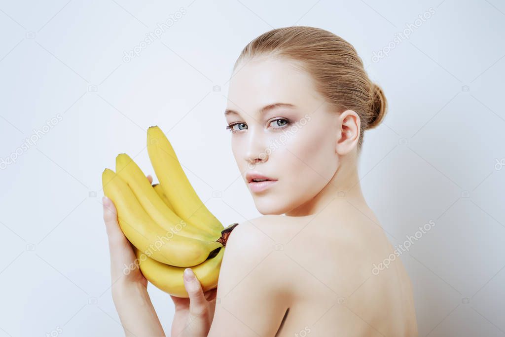 Beauty, natural cosmetics concept. Beautiful young woman with healthy shiny skin holding bananas. White background. 