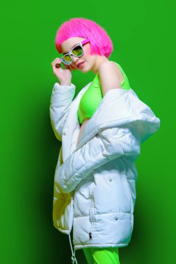 Trendy kız pembe saçlı parlak şık kıyafetler giyiyor. Yeşil arka plan. Güzellik, moda, gençlik tarzı.