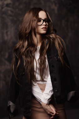 Modern gençlik giyim ve gözlük çekici genç bir kadın portresi. Stüdyo koyu arka plan üzerinde vurdu. Güzellik, moda kavramı.