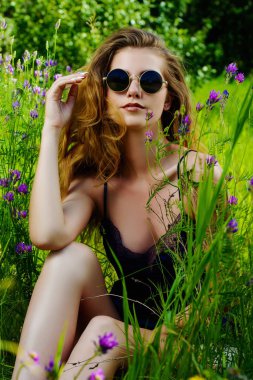 Güzel kız kır çiçekleri arasında çim oturuyor. Yaz günü. Modern hippi, hippi tarzı. Güzellik, moda açık.
