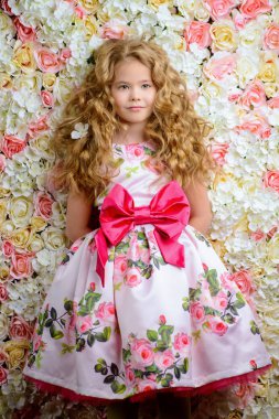 Güzel bir yaz, sevimli küçük bir kız portresi elbise sarı kıvırcık saçlı. Arka plan gül. Çocuk Moda, stil.