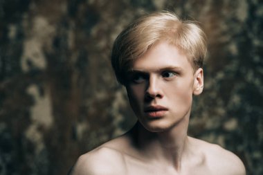 Portre gömleksiz bir gencin stüdyoda grunge arka plan üzerinde poz sarışın saçlı. Erkek güzellik ve sağlık.