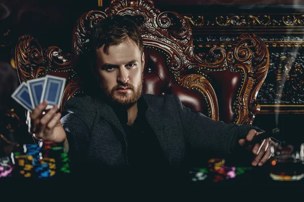 A wealthy mature man smoking cigar and playing poker in a casino. Gambling, playing cards and roulette.