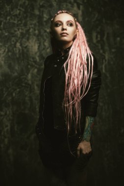 Kadın modeli pembe dreadlocks karanlık bir arka plan üzerinde poz ile çarpıcı. Son moda saç modelleri. Güzellik, moda. 