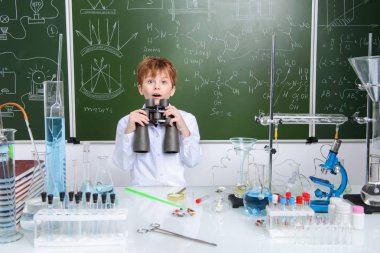 Okul çocuğu dürbün ile bir kimya ders tarafından yazı tahtası görünüyor. Eğitim kavramı.
