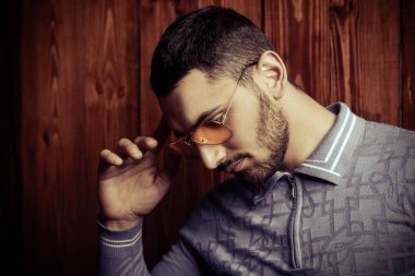 Vogue bir T-shirt ve ahşap bir duvarın ardında duran sarı güneş gözlüğü yakışıklı bir erkek model bir kadeh. Erkek güzelliği, moda. 