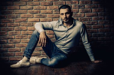 Bir tuğla duvar tarafından poz yakışıklı bir brunet adam portresi. Erkek güzelliği, moda. Erkek Berber Dükkanı, saç modeli.