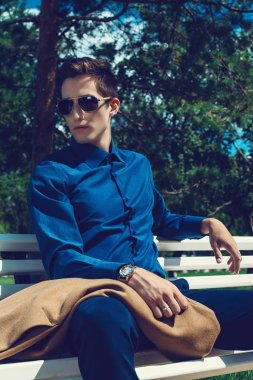 Şık giysiler içinde yakışıklı bir genç adam ve güneş gözlüğü yaz Park portresi. Moda vurdu. İş tarzı. 