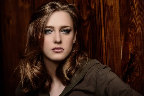 Beautiful young woman with natural makeup standing by a wooden wall. Beauty, fashion concept. Hair styling.