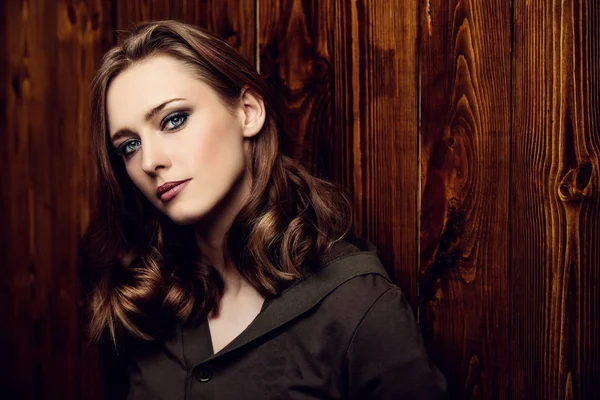 Beautiful young woman with natural makeup standing by a wooden wall. Beauty, fashion concept. Hair styling.