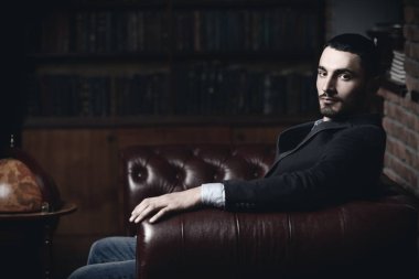 Deri koltuk üzerinde seksi yakışıklı bir adam portresi. Moda vurdu. Erkek güzelliği, moda. Erkek Berber Dükkanı, saç modeli.