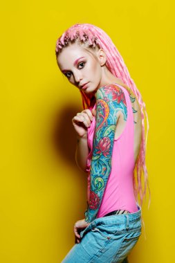 Sarı arka planda parlak elbiseler giymiş pembe rastalı şık bir kız. Güzellik, moda.