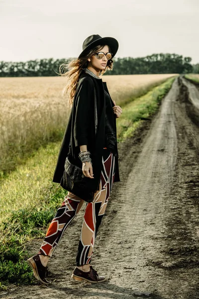 Fashionable young woman walking on a country road. Autumn and spring style.
