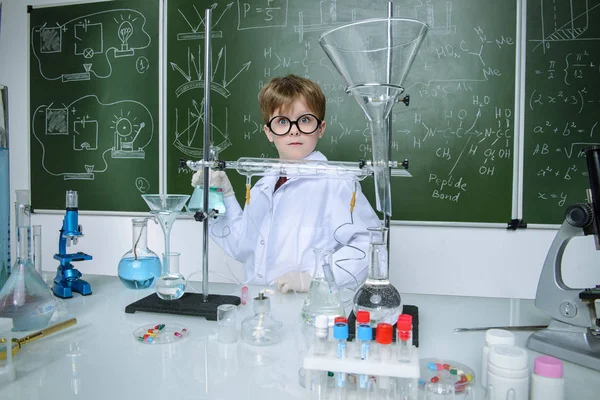 Clever schoolboy stands by a chalkboard on a chemistry lesson. Educational concept.