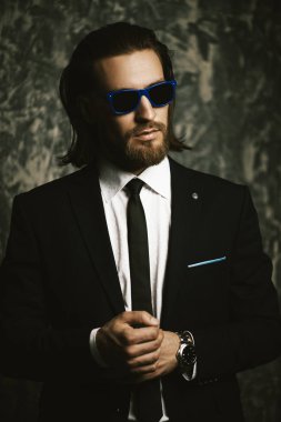 Moda vurdu. Şık takım elbise ve güneş gözlüğü koyu arka plan üzerinde poz yakışıklı delikanlı. Erkek güzelliği, moda.