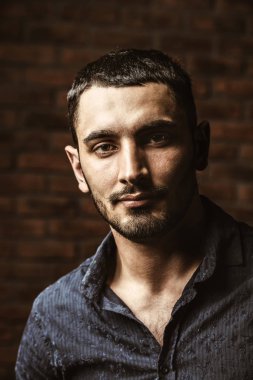 Yakışıklı bir brunet adam ayakta bir tuğla duvar tarafından portresi. Erkek güzelliği, moda. Erkek Berber Dükkanı, saç modeli.