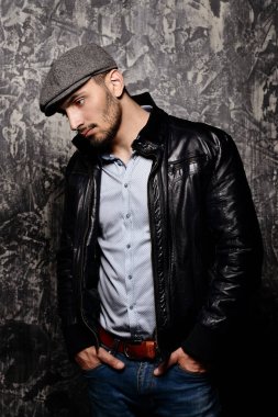Grunge arka plan üzerinde bir kap ve deri ceketli yakışıklı bir adam portresi. Stüdyo vurdu. Erkek güzelliği, moda. Erkek berber.