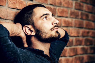 Yakışıklı bir brunet adam ayakta bir tuğla duvar tarafından portresi. Erkek güzelliği, moda. Erkek Berber Dükkanı, saç modeli.