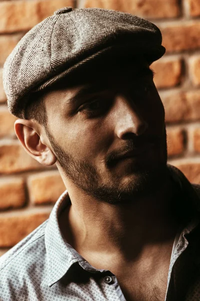 Portrait of a handsome brunet man in a cap over brick wall background. Men\'s beauty, fashion. Men\'s barbershop.