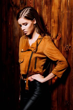 Genç ve güzel kadın kahverengi bir ceket ve ahşap duvar tarafından poz deri pantolon. Gençlik stil, moda.