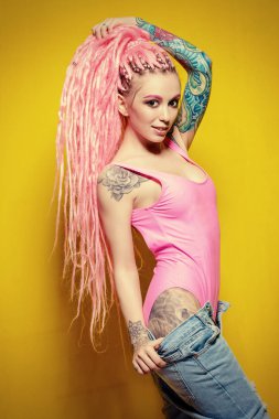 Sarı arka planda parlak elbiseler giymiş pembe rastalı şık bir kız. Güzellik, moda.