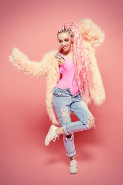 Şık kız pembe dreadlocks pembe bir arka plan üzerinde parlak giysiler içinde poz ile. Tam uzunlukta portre. Güzellik, moda.