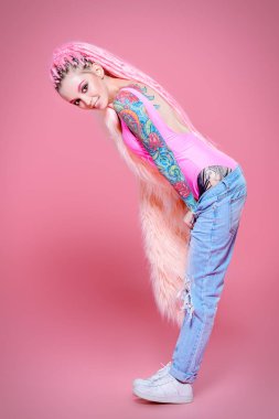 Şık kız pembe dreadlocks pembe bir arka plan üzerinde parlak giysiler içinde poz ile. Tam uzunlukta portre. Güzellik, moda.