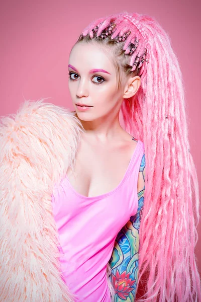Şık kız pembe dreadlocks pembe bir arka plan üzerinde parlak giysiler içinde poz ile. Güzellik, moda.