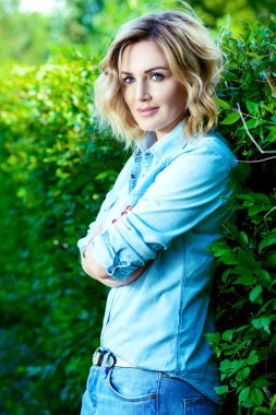 Güzel orta yaşlı kadın bir yaz günü parkta yeşil çit tarafından duruyor. Güzellik, kozmetik.