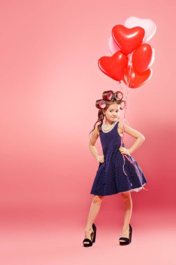 Annenin Ayakkabı ve balonlar saçında curlers ile garip bir küçük kız portresi. Stüdyo pembe arka plan üzerinde vurdu. Çocuk moda. 