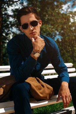Şık giysiler içinde yakışıklı bir genç adam ve güneş gözlüğü yaz Park portresi. Moda vurdu. İş tarzı. 