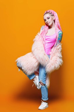 Şık kız pembe dreadlocks sarı bir arka plan üzerinde parlak giysiler içinde poz ile. Tam uzunlukta portre. Güzellik, moda.