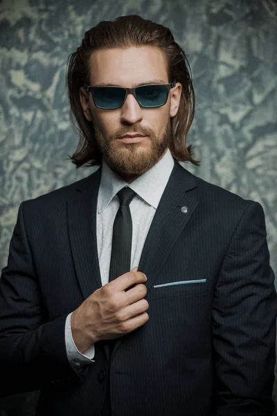 Moda vurdu. Şık takım elbise ve güneş gözlüğü koyu arka plan üzerinde poz yakışıklı delikanlı. Erkek güzelliği, moda.