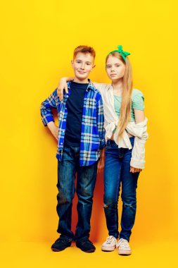 Mutlu çocuk ve kız parlak sarı zemin üzerinde tam uzunlukta portre. Çocuk moda.
