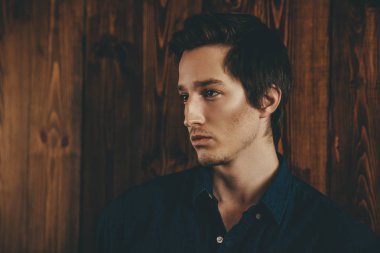 Vogue bir ahşap duvar bir kot gömlek bekliyor yakışıklı bir erkek modelinde bir kadeh. Erkek güzelliği, moda. 