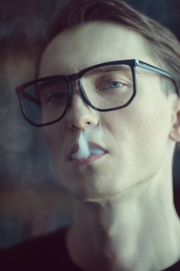Düşünceli ve sakin bir şekilde sigara çekici bir genç adam. Erkek güzelliği, moda. Optik stili.