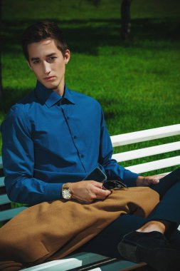 Heybetli yakışıklı genç bir parkta bir bankta oturuyor. Moda vurdu. İş tarzı. 