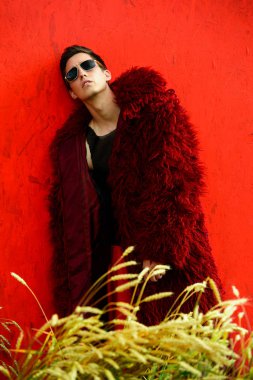 Profesyonel bir yakışıklı erkek model kırmızı uzun kürk ceket buğday alanında poz moda çekim. 