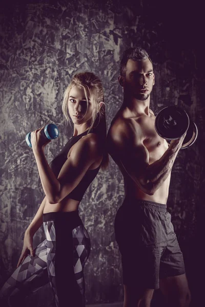 Couple of muscular young people doing exercises with dumbbells. Fitness, bodybuilding. Active, healthy lifestyle.