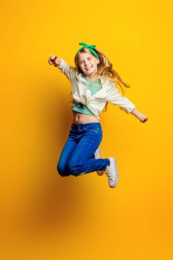 Çocuk moda. Stüdyoda sarı arka plan üzerinde atlama sarı elbiseli güzel küçük kız.