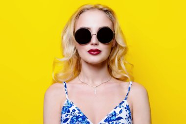 Çekici genç kadın sarı arka plan üzerinde parlak giysiler ve güneş gözlüğü takıyor. Parlak stil, moda. Optik stili. 