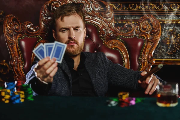 A wealthy mature man smoking cigar and playing poker in a casino. Gambling, playing cards and roulette.