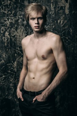 Portre gömleksiz bir gencin stüdyoda grunge arka plan üzerinde poz sarışın saçlı. Erkek güzellik ve sağlık.