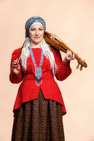 Elderly native woman in a national costume plays the ancient violin.