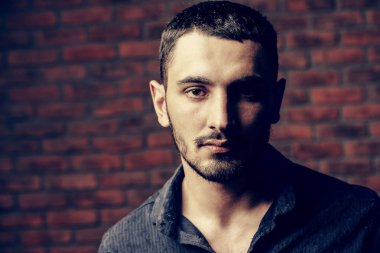 Yakın çekim portre yakışıklı bir brunet adamın üzerinde tuğla duvar arka plan. Erkek güzelliği, moda. Erkek Berber Dükkanı, saç modeli.