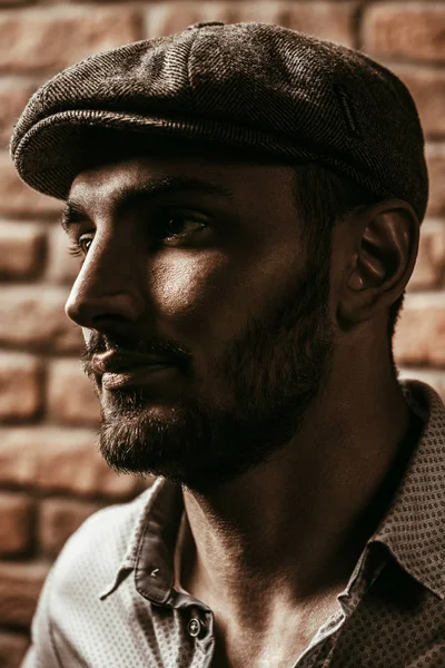 Portrait of a handsome brunet man in a cap over brick wall background. Men's beauty, fashion. Men's barbershop.