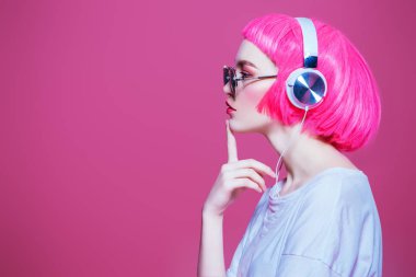 Trendy girl with pink hair wearing sunglasses enjoys the music on headphones. Pink background. Youth style, leisure. clipart